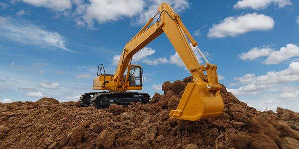A yellow excavator digging soil under a blue sky.