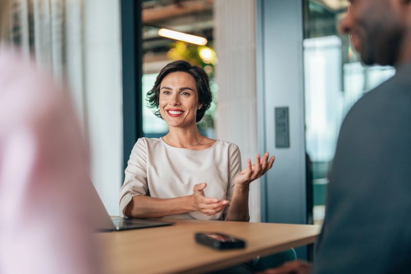 Dynamic professional interaction between colleagues in a modern, collaborative workspace. With a modern technology in use, the setting suggests a focused discussion—possibly a performance review, strategic planning session, or client consultation.