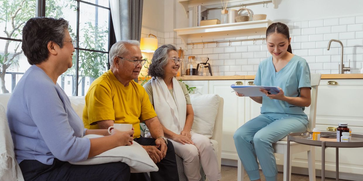 A nurse in scrubs consulting three elderly people in a cozy living room.