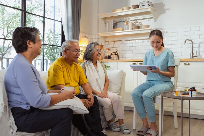 Healthy Asian senior couple receives compassionate healthcare consultation as professional doctor and nurse discuss personalized treatment plan and wellness monitoring in comfortable nursing home environment