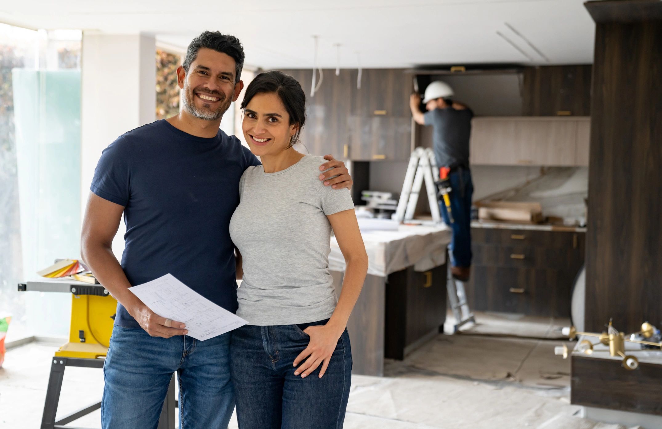 Smiling couple with blueprints in kitchen renovation.