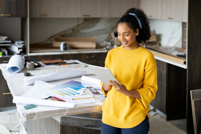 Happy African American interior designer remodeling a kitchen and using a digital tablet while smiling