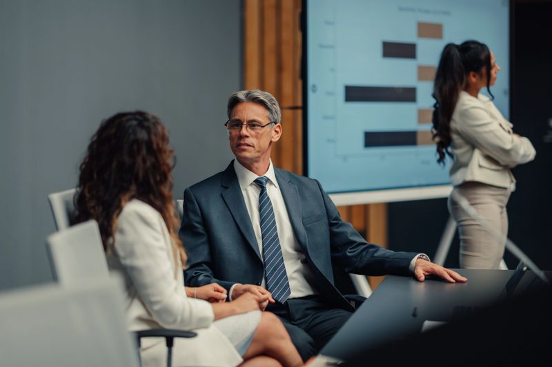 Business professionals engaging in a focused discussion in a modern conference room, reviewing data on a presentation screen
