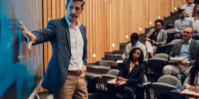A man presenting information to an attentive audience in a lecture hall.
