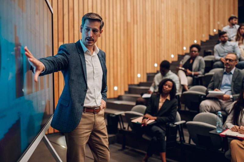 Business speaker giving presentation on a large screen to a diverse group of professionals and students in an auditorium