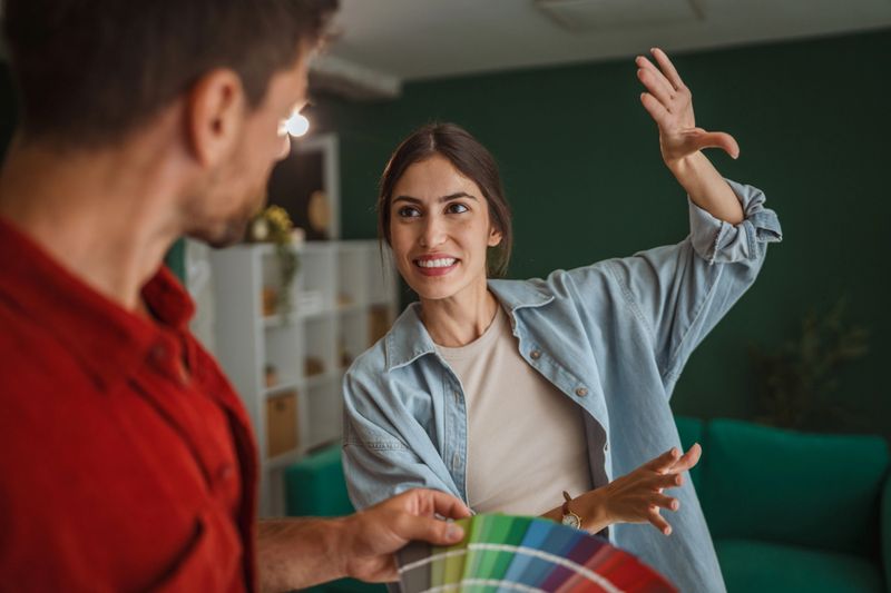 Young couple comparing paint swatches and planning interior colors for a cozy modern living room during a home renovation, smiling and discussing design ideas and future plans