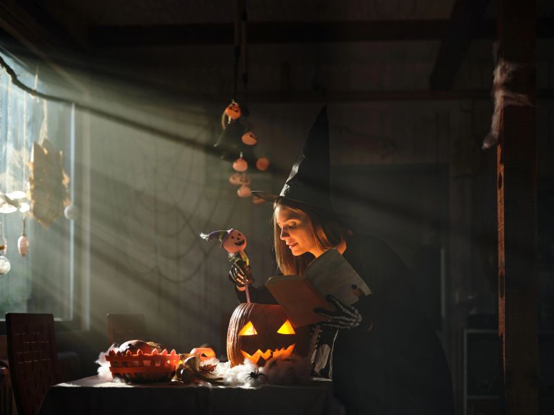 Smiling witch casting a spell on Jack O' Lantern during Halloween in dining room.