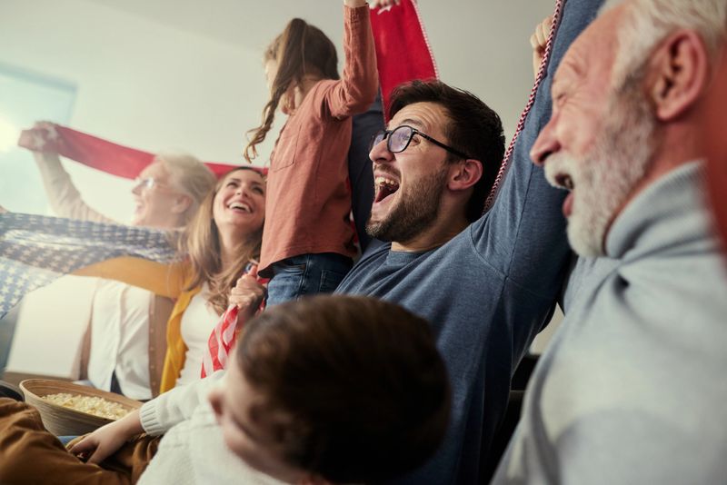 Cheerful multi-generation family having fun while watching a game of their favorite sports team on TV at home.