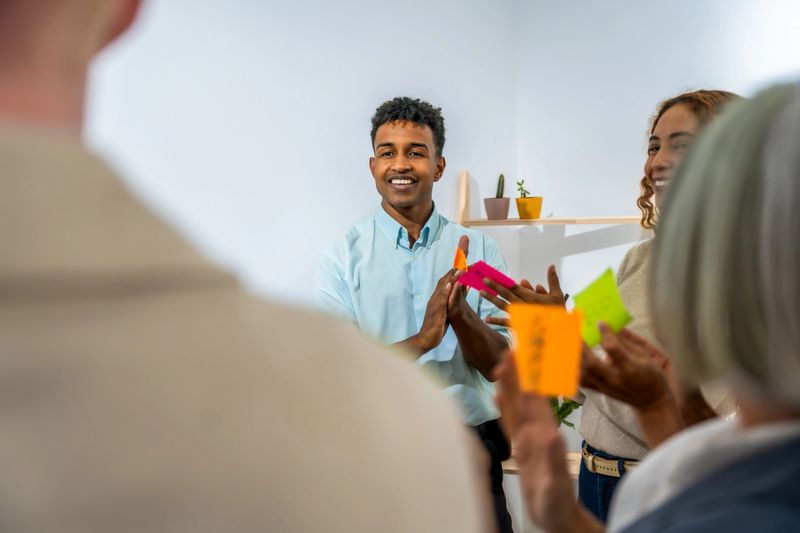 Group of multi-ethnic professionals, including young adults, mid adults, and senior adults, engaged in a creative brainstorming session, holding colorful sticky notes