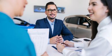 A couple consulting a car salesman in a showroom.