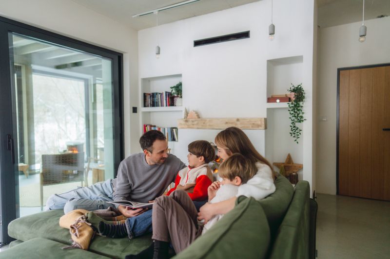 Photo of a cheerful young family, sitting in their cosy living room, by the fireplace, reading books and enjoying each others company