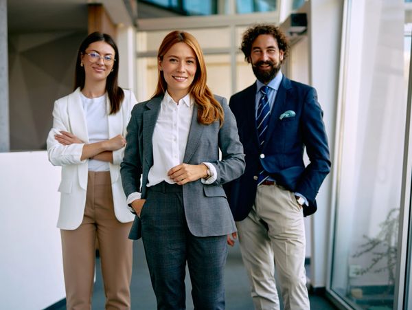 Three confident professionals posing in a modern office hallway.