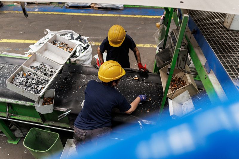 Two workers working on conveyor belt in recycling center, sorting metal in plastic boxes, high angle view