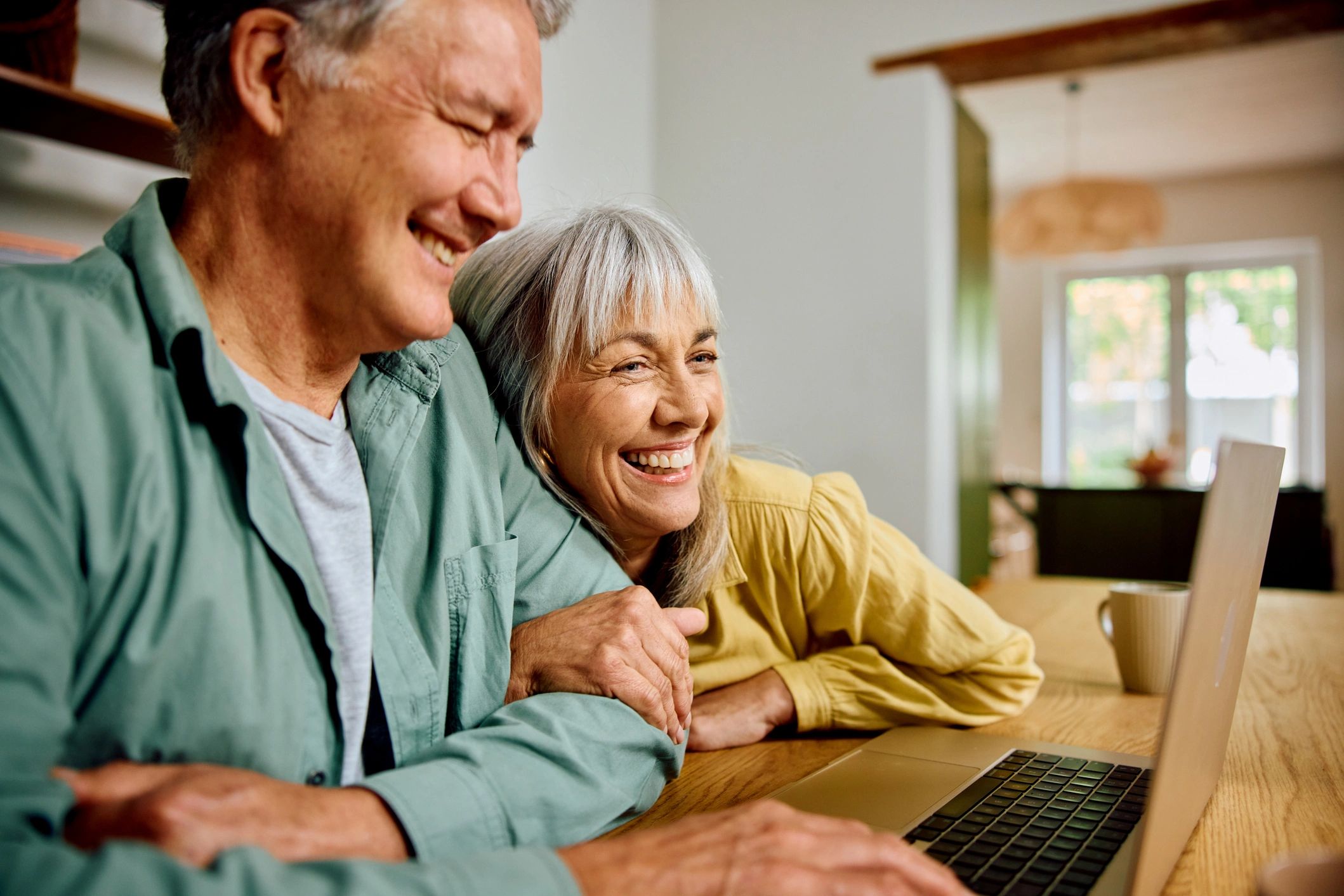 Older couple smiling while reviewing information on a laptop at home | Family First Financial 
