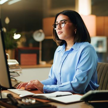 Woman in blue blouse working focused at her desk with a computer.