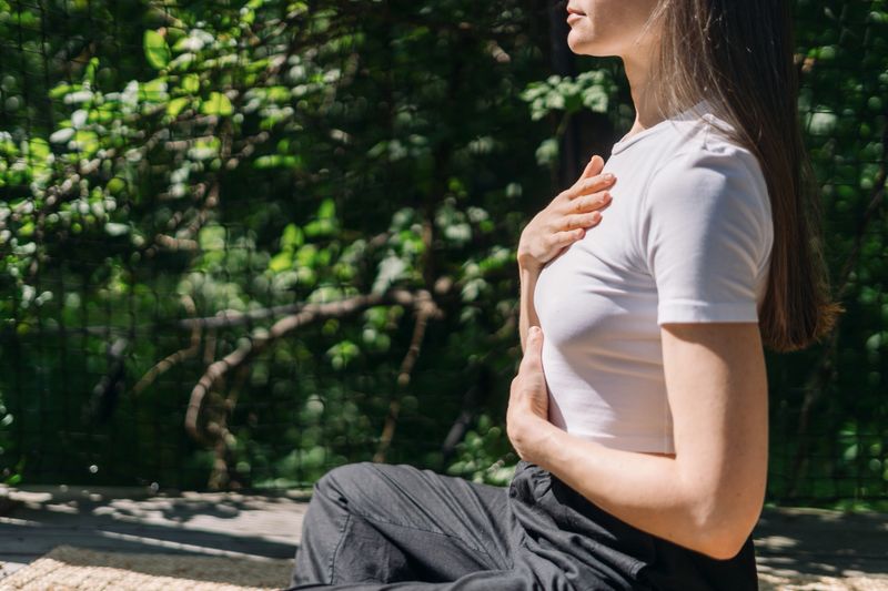 Serene woman sits in park outdoors, engaging in deep breathing exercise and yoga practice. Calm and mindfulness moment at summer day. Person meditate, connects with nature in the morning light.