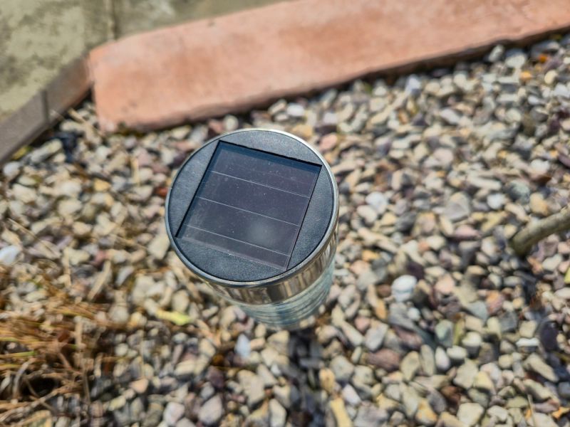Close-up of a solar-powered garden light installed on pebbles, showcasing modern outdoor lighting technology and eco-friendly energy use for landscaping at daytime.