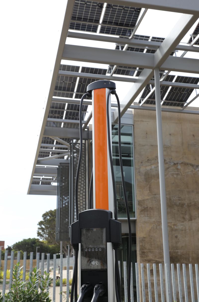 A modern building equipped with solar panels with electric charging station right by it.