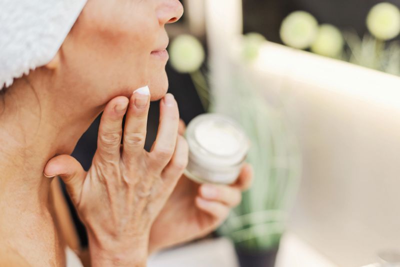 A woman applies facial cream with care, showcasing skincare, self-care, and beauty routines in a calm, intimate bathroom scene.