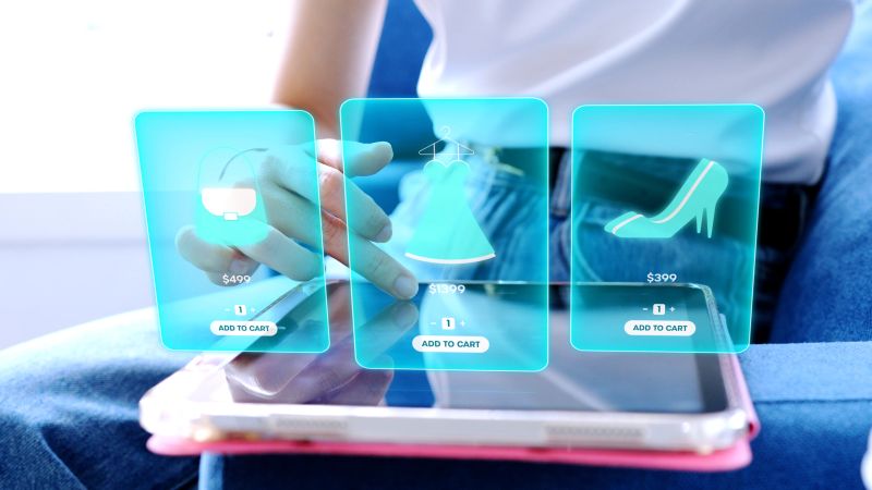 Woman using tablet with futuristic augmented reality (AR) interface for online fashion shopping, choosing products to add to cart, concept of e-commerce, metaverse, and retail technology.