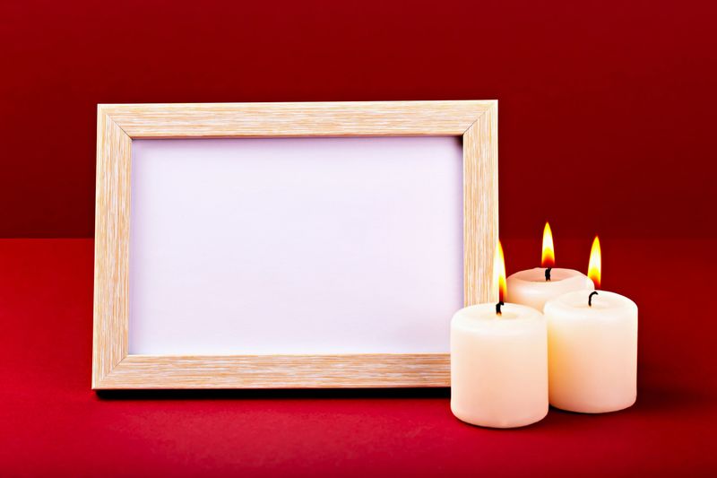 Mockup. Elegant wooden frame featuring blank with copy space is positioned next to three lit candles, creating warm and inviting atmosphere against vibrant red backdrop