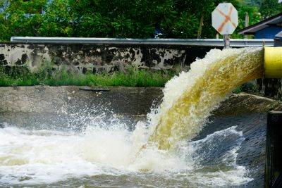 Water flows forcefully from a pipe into a river or canal.