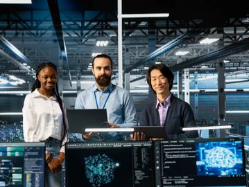Three tech professionals collaborating in a modern data center with multiple monitors displaying AI data.