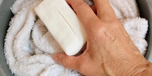 Hand holding a white bar of soap over a fluffy white towel.