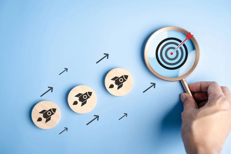 Ambition and goal achievement concept with rocket icons aiming at target through magnifying glass, business growth, success, mission focus, startup launch, and strategic vision.