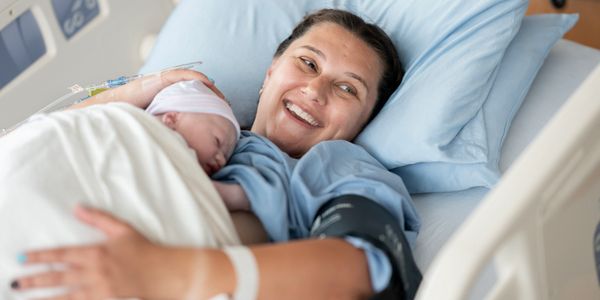 A joyful mother lying in a hospital bed holding her newborn baby close.