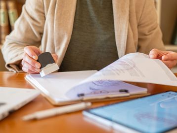 Person stamping documents at a desk with office supplies nearby.