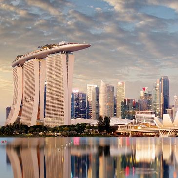 Marina Bay Sands and Singapore skyline reflected in calm water at dusk.