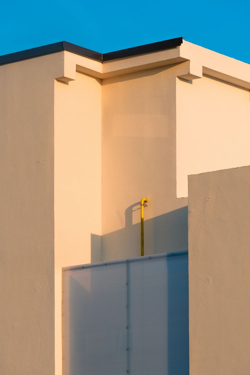 Minimalist architecture detail of modern building facade illuminated by warm sunset light, geometric shapes and clean lines against clear blue sky. Selective focus.