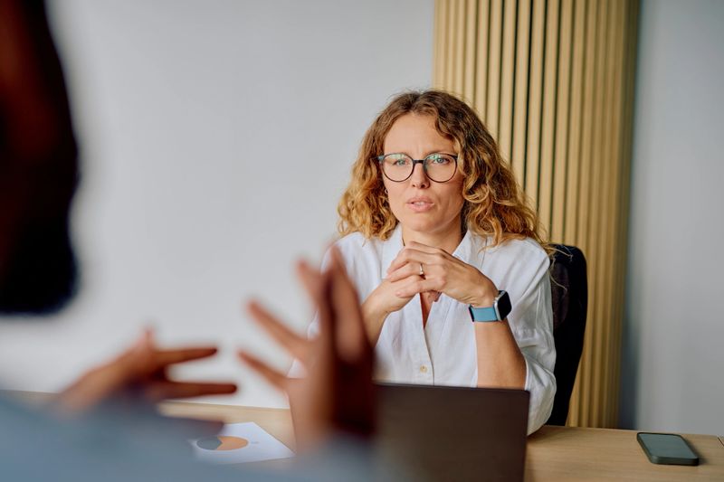 Businesswoman with curly hair listening intently, clasping hands while attending a corporate meeting or discussion in an office