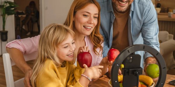 Family holding apples and smiling at a phone camera for a video call.