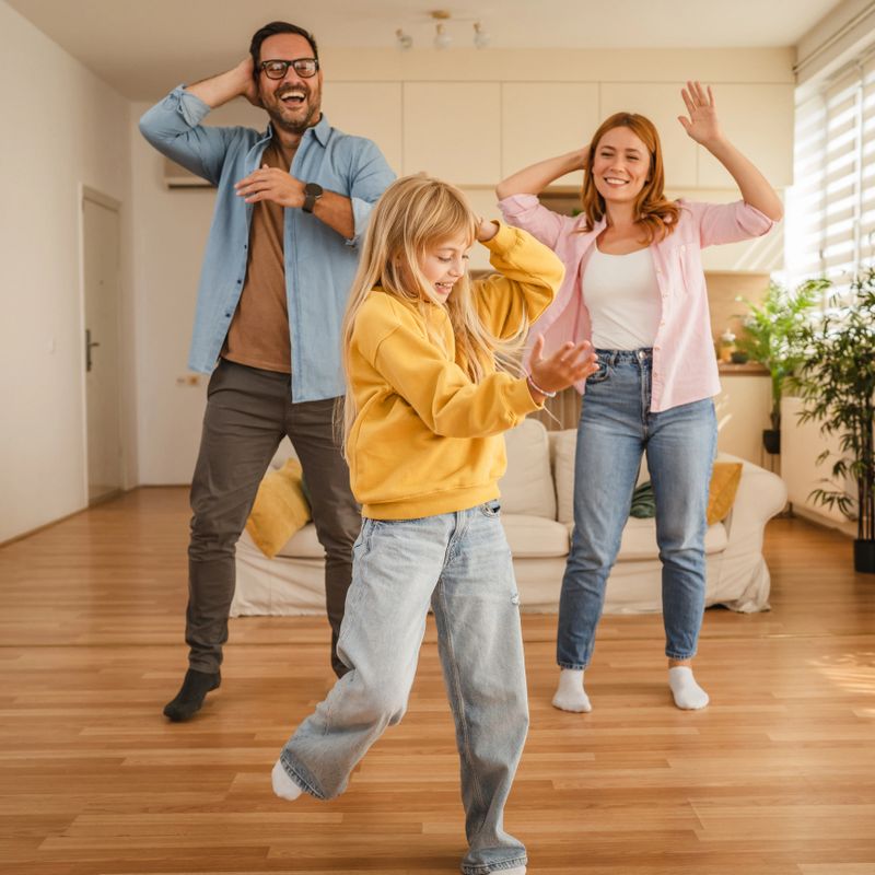 Happy family, a father, mother, and child, dancing with energy and having fun at home, sharing joyful moments and strengthening their bond in a bright living space