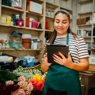 Florist checks tablet in a flower shop surrounded by colorful blooms.