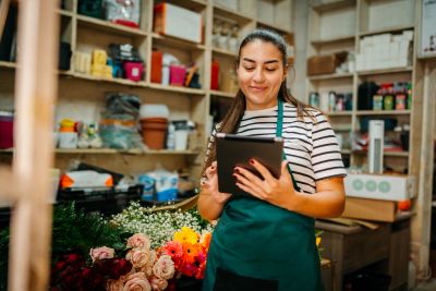 A florist using a tablet in a flower shop surrounded by colorful flowers.
