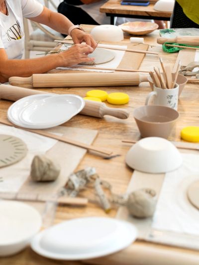 Hands shaping clay on a pottery workspace with tools and plates.