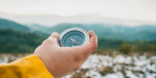 Person holding a compass with a mountainous landscape in the background.