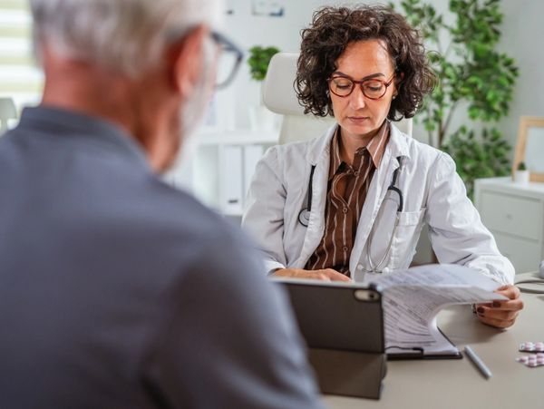 Doctor reviewing medical documents while consulting an elderly patient.