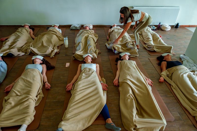 A group of people relaxing under blankets during a guided meditation session in a serene yoga studio. The scene features participants with eye masks, cozy mats, and a calming environment with natural light, perfect for wellness, stress relief, and mindfulness content. High-resolution stock photo ideal for health blogs, spa advertising, or mental health resources