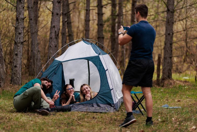 Four friends relax and have fun while camping in a serene forest setting. They pose playfully inside the tent, enjoying each others company amidst nature.