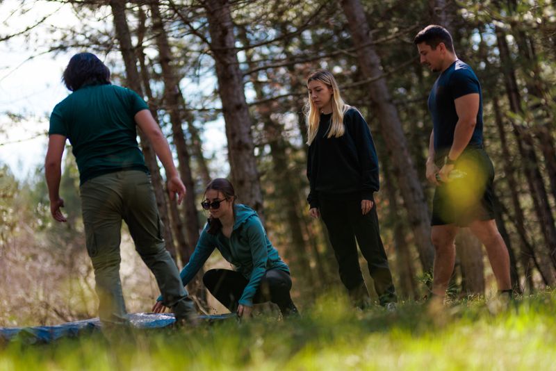 Group of friends working together to set up a tent in the woods. Sunlight filters through the trees, creating a cheerful atmosphere as they prepare for their outdoor adventure.