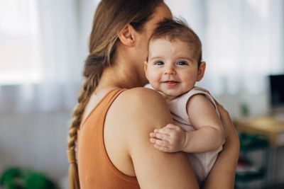 Smiling baby being held by mother with braided hair indoors.