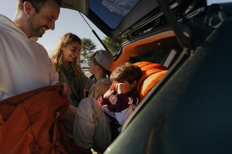 Photo of a smiling, cheerful family packing up in the trunk of their car for an autumn adventure to the nearest beach