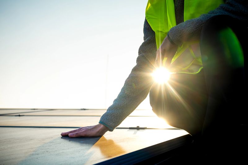 Female technician hand on solar panel on factory rooftop featuring bright sunlight and industrial environment highlighting renewable energy efforts.