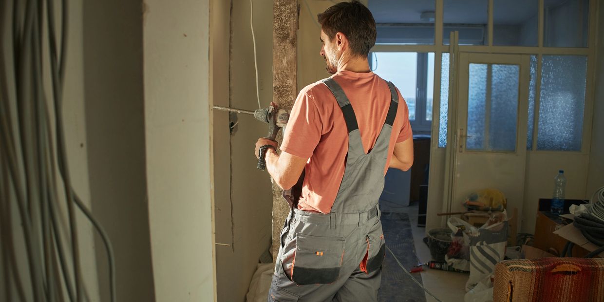 Worker drilling a wall in a room under renovation.
