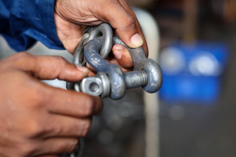 Close up technician hand holding and tighten the shackle pins attached to the chain.