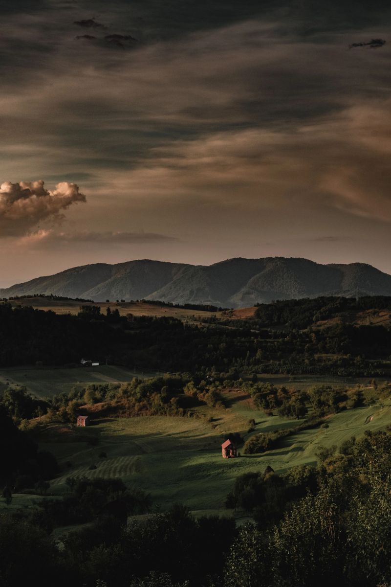 Scenic view of a serene valley with lush greenery and distant mountains under a dramatic sky at dusk.